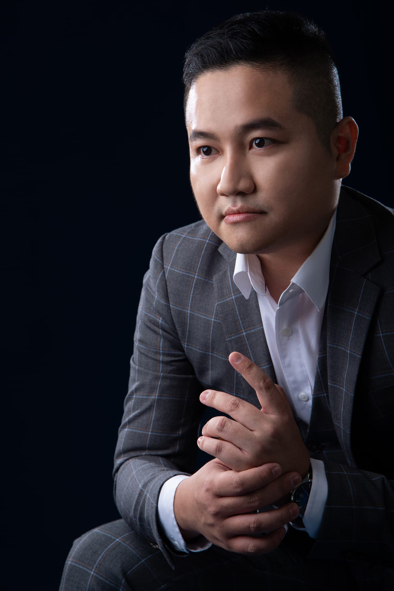 深蓝背景前，Kevin 坐着，双手轻轻交握，专注地看向镜头。